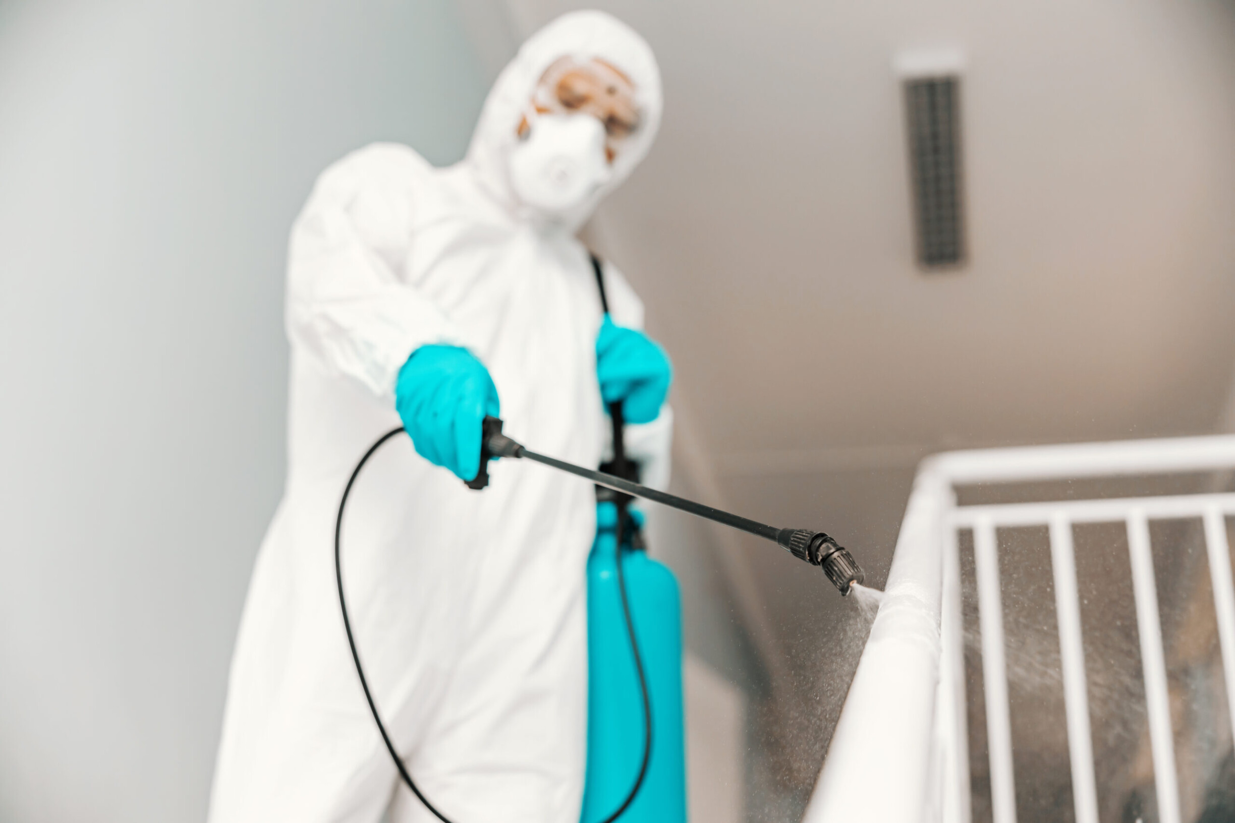 closeup-of-worker-in-sterile-uniform-with-gloves-and-facial-mask-sterilizing-railing-in-school-scaled.jpg